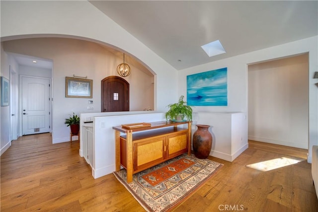 hallway featuring a skylight, arched walkways, baseboards, and light wood-style floors