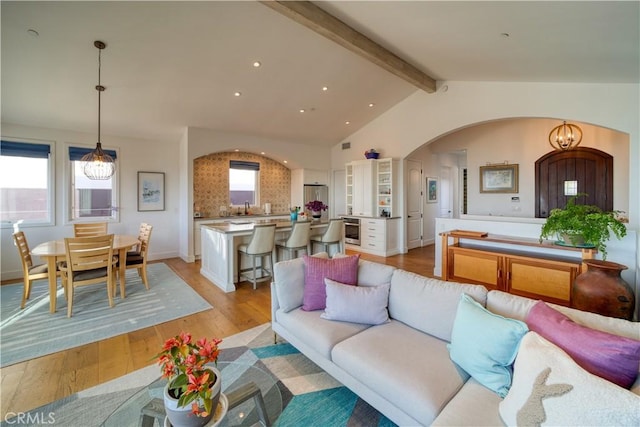 living area featuring recessed lighting, arched walkways, vaulted ceiling with beams, and light wood finished floors