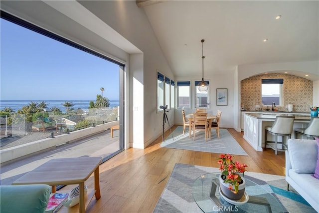 interior space featuring light wood finished floors, recessed lighting, baseboards, lofted ceiling, and a water view