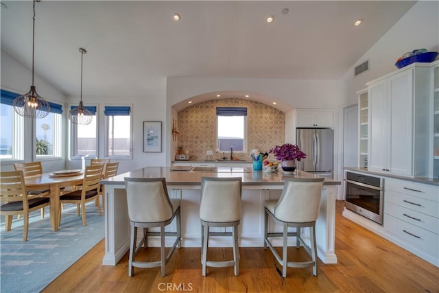 kitchen with backsplash, a kitchen bar, visible vents, white cabinets, and stainless steel appliances
