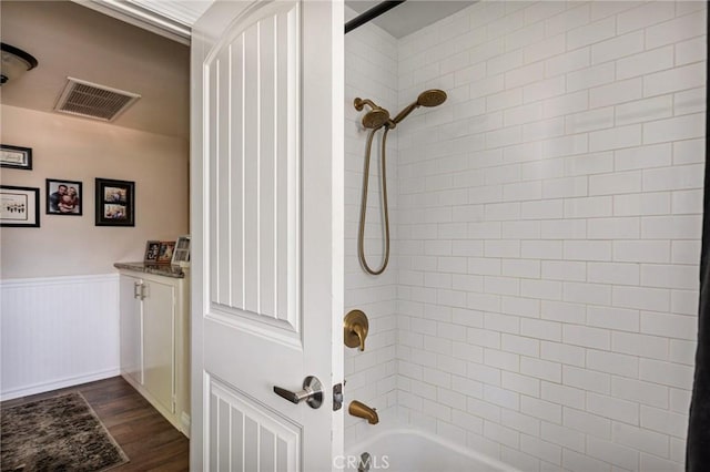full bathroom with a wainscoted wall, bathing tub / shower combination, wood finished floors, and visible vents