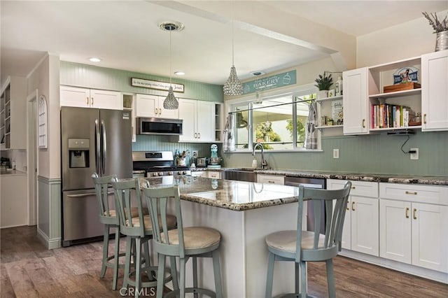 kitchen with open shelves, a kitchen bar, dark stone counters, a sink, and stainless steel appliances