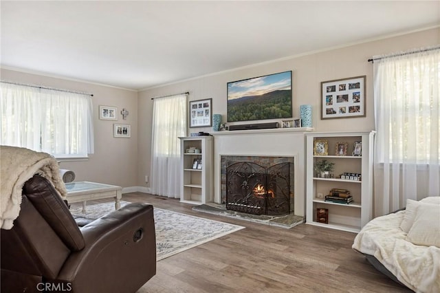 living room featuring crown molding, baseboards, a lit fireplace, and wood finished floors