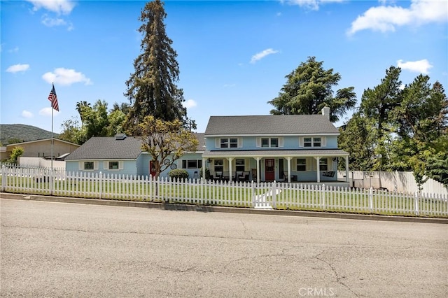 farmhouse-style home with covered porch, a fenced front yard, and a front lawn