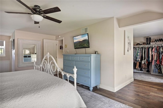 bedroom with ceiling fan, a walk in closet, baseboards, visible vents, and dark wood-style floors