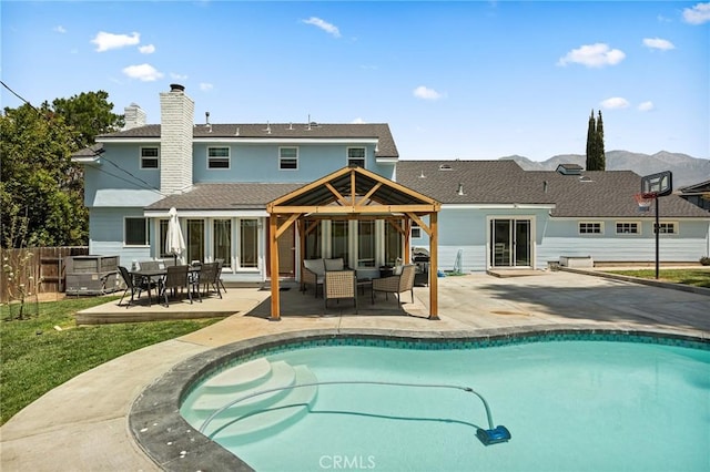 back of property featuring fence, a patio, a chimney, a fenced in pool, and a shingled roof