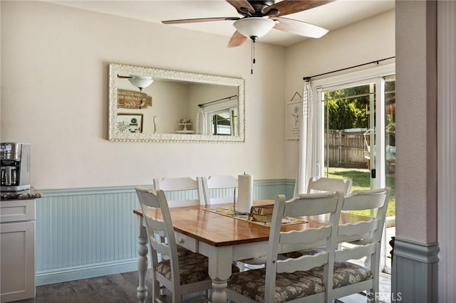dining space featuring dark wood finished floors, ceiling fan, and wainscoting