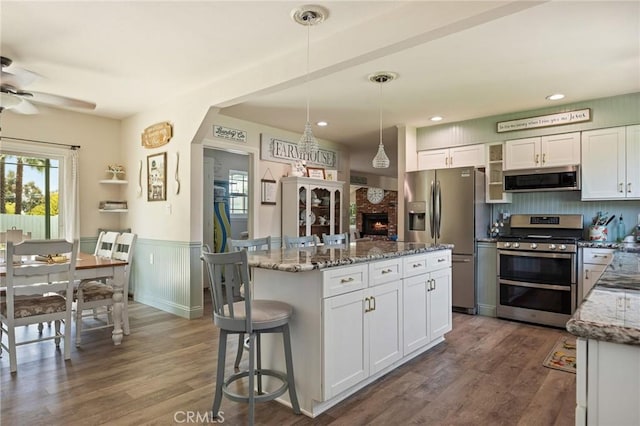 kitchen featuring white cabinets, ceiling fan, light stone counters, wainscoting, and stainless steel appliances