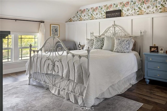 bedroom featuring a decorative wall, a wainscoted wall, wallpapered walls, wood finished floors, and lofted ceiling