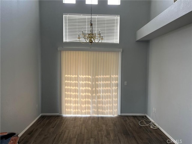 unfurnished living room with baseboards, a wealth of natural light, wood finished floors, and a chandelier