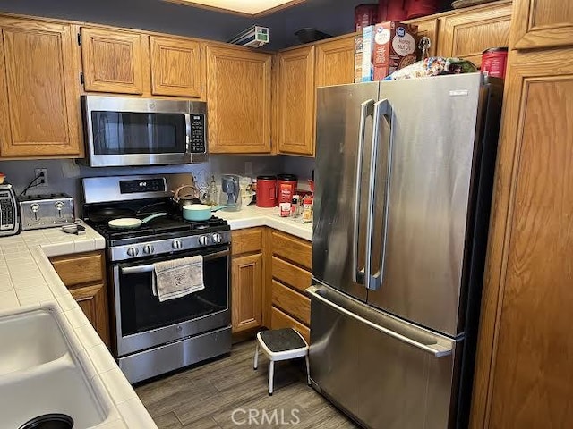 kitchen with a sink, appliances with stainless steel finishes, tile countertops, and light wood-style flooring
