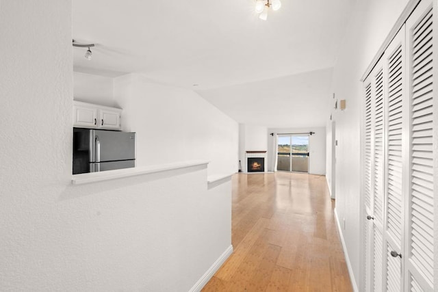 hall featuring light wood-type flooring, baseboards, and vaulted ceiling