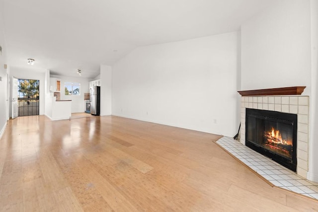 unfurnished living room with light wood-type flooring, vaulted ceiling, and a tile fireplace