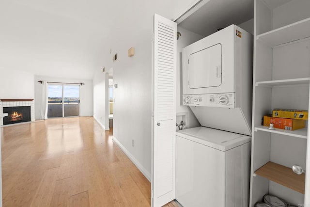 washroom with laundry area, stacked washer / dryer, a fireplace, baseboards, and light wood-style flooring