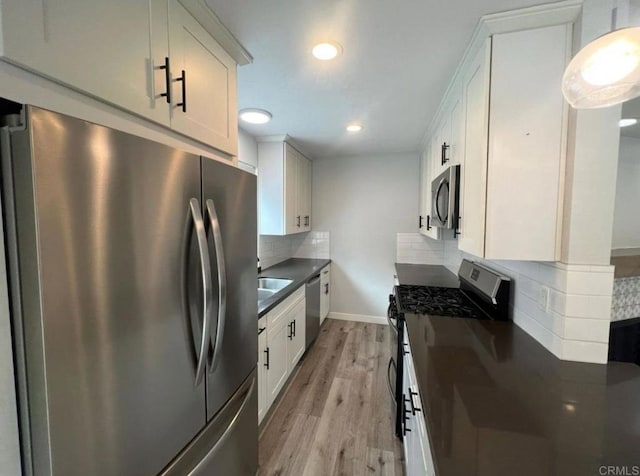 kitchen with dark countertops, appliances with stainless steel finishes, light wood-style flooring, baseboards, and backsplash