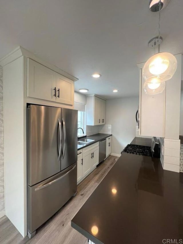 kitchen with stainless steel appliances, dark countertops, a sink, and light wood finished floors