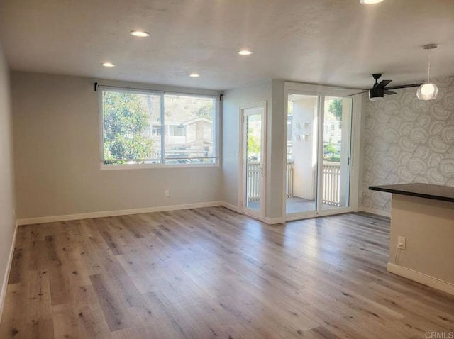 unfurnished living room with a ceiling fan, wallpapered walls, recessed lighting, baseboards, and wood finished floors