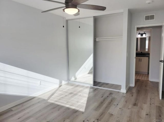 unfurnished bedroom featuring ceiling fan, light wood-style floors, baseboards, visible vents, and a closet