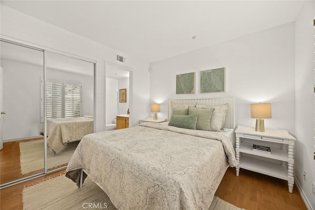 bedroom with visible vents, wood finished floors, baseboards, a closet, and ensuite bathroom