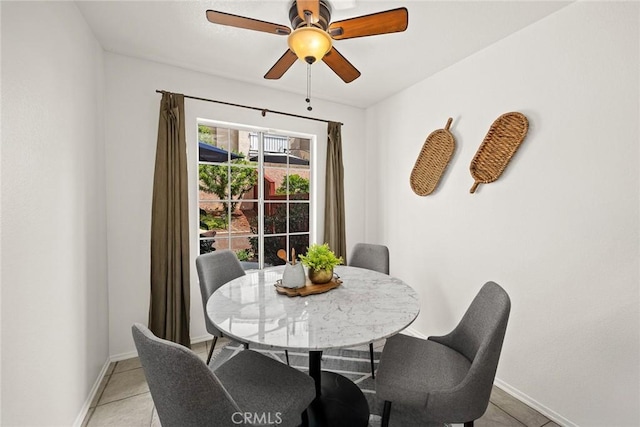dining space with a ceiling fan, baseboards, and light tile patterned floors