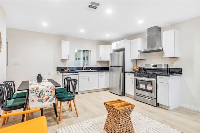 kitchen featuring wall chimney range hood, stainless steel appliances, light wood-type flooring, and a sink