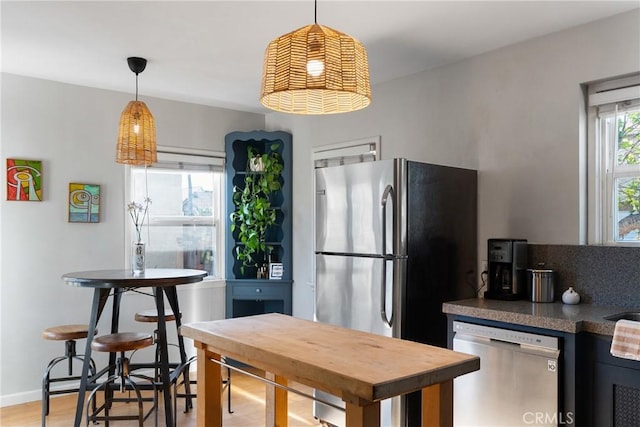 kitchen featuring baseboards, light wood finished floors, decorative light fixtures, and stainless steel appliances
