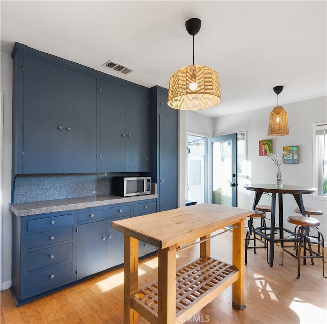 kitchen with stainless steel microwave, visible vents, blue cabinets, and light wood-type flooring