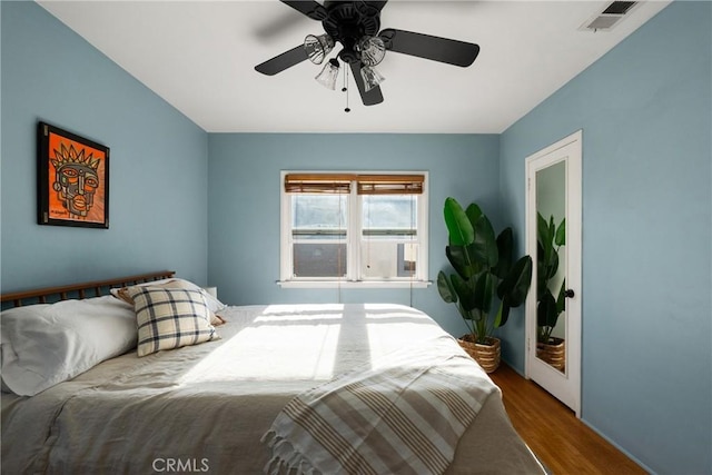 bedroom featuring baseboards, a ceiling fan, wood finished floors, and visible vents