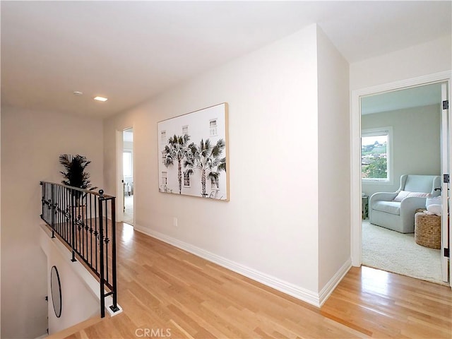 corridor featuring light wood-style floors, baseboards, recessed lighting, and an upstairs landing