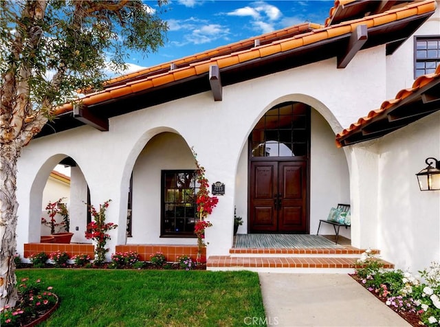 property entrance with a lawn, a tiled roof, and stucco siding
