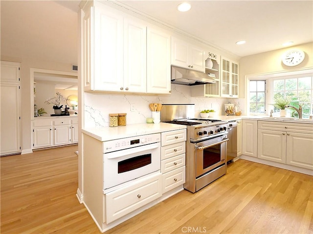 kitchen featuring appliances with stainless steel finishes, light wood-type flooring, a sink, under cabinet range hood, and white cabinetry