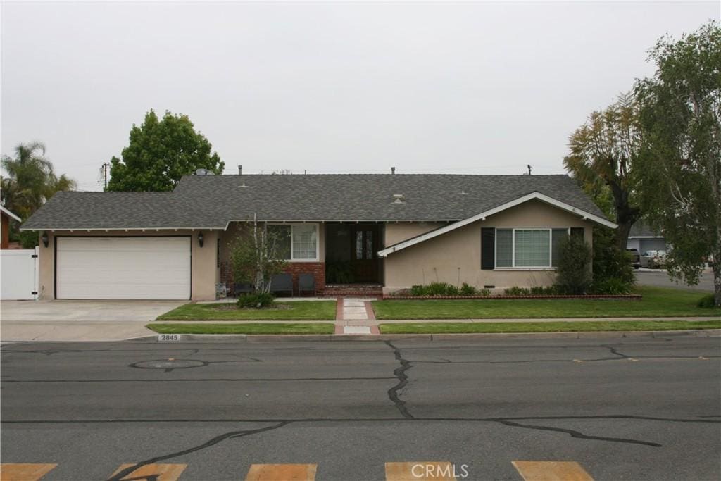 single story home with driveway, a front yard, a garage, a shingled roof, and stucco siding