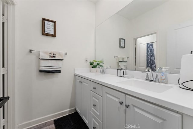 bathroom with double vanity, a sink, baseboards, and wood finished floors
