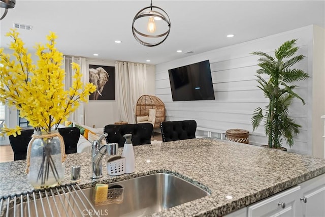kitchen with visible vents, a sink, light stone counters, white cabinets, and recessed lighting