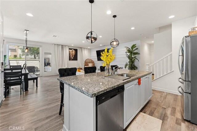 kitchen with a kitchen island with sink, appliances with stainless steel finishes, a sink, light wood finished floors, and open floor plan