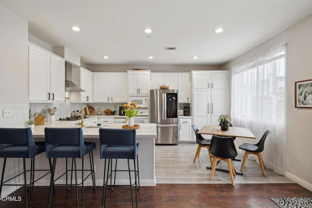 kitchen with visible vents, a peninsula, smart refrigerator, white microwave, and wall chimney range hood