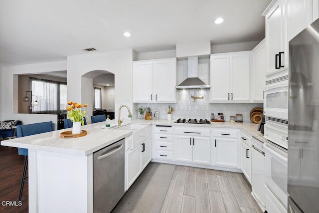 kitchen with visible vents, a sink, wall chimney exhaust hood, arched walkways, and stainless steel appliances