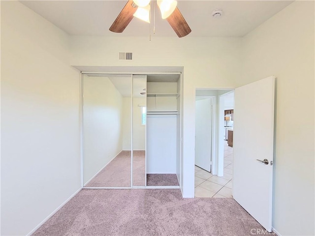 unfurnished bedroom featuring light carpet, a ceiling fan, light tile patterned floors, visible vents, and a closet