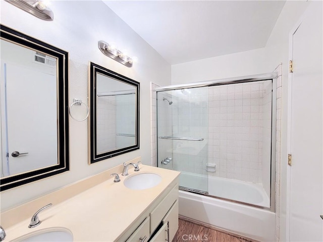 bathroom with double vanity, a sink, wood finished floors, and bath / shower combo with glass door