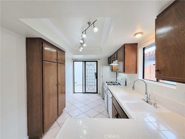 kitchen with crown molding, gas range gas stove, a sink, tile counters, and a tray ceiling