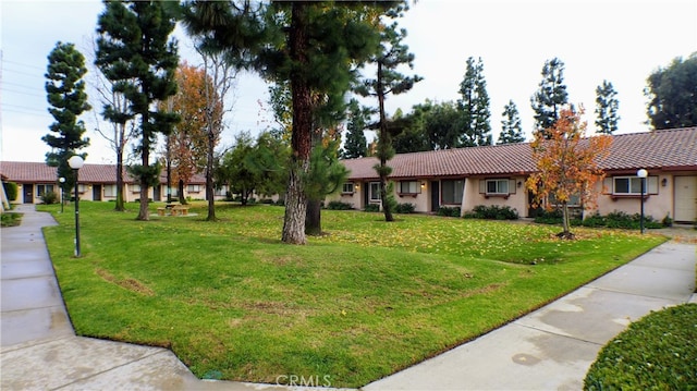 ranch-style house with a tiled roof, stucco siding, and a front lawn