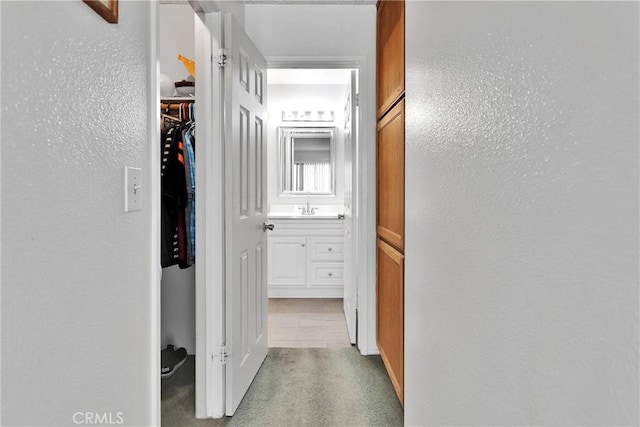 hall with a sink, a textured wall, and carpet