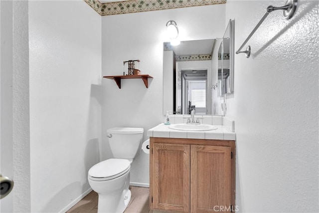 half bathroom featuring toilet, baseboards, wood finished floors, and vanity