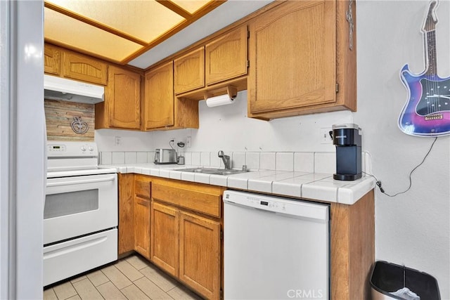 kitchen with white appliances, under cabinet range hood, brown cabinetry, and a sink