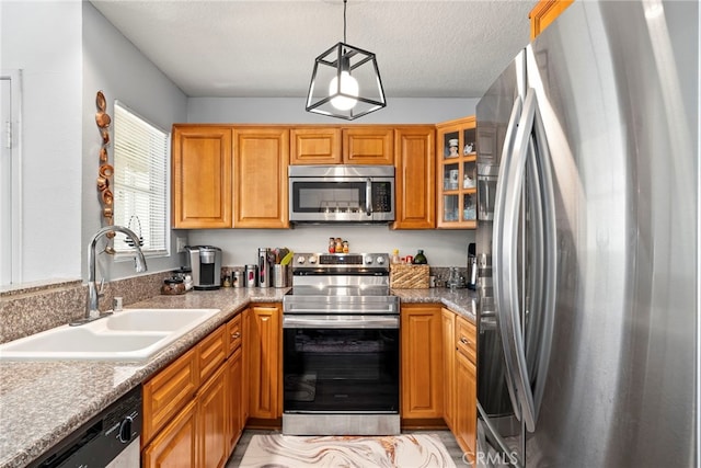 kitchen with brown cabinetry, glass insert cabinets, a sink, appliances with stainless steel finishes, and decorative light fixtures