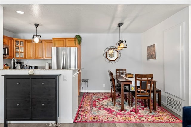kitchen featuring light stone countertops, brown cabinetry, stainless steel appliances, visible vents, and glass insert cabinets