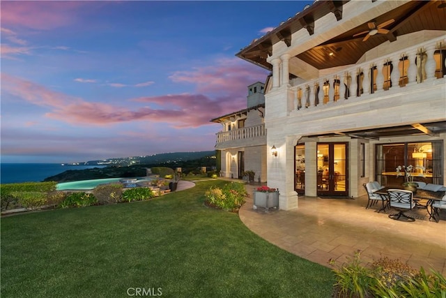 yard at dusk featuring a patio, a ceiling fan, french doors, and a balcony
