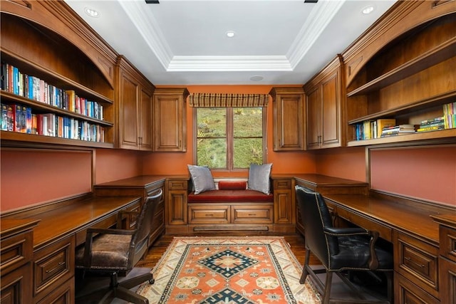 home office featuring a tray ceiling, ornamental molding, wood finished floors, and built in study area