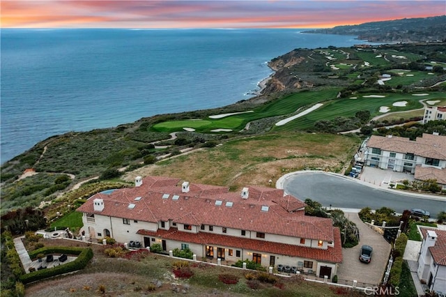 aerial view at dusk featuring a water view and golf course view