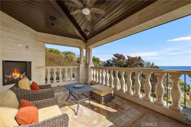 balcony with a water view, a fireplace, and a ceiling fan
